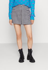 Gonna corta bianco e nero a motif houndstooth con zip frontale. Abbinata a un maglione azzurro texturizzato e stivaletti neri con lacci.