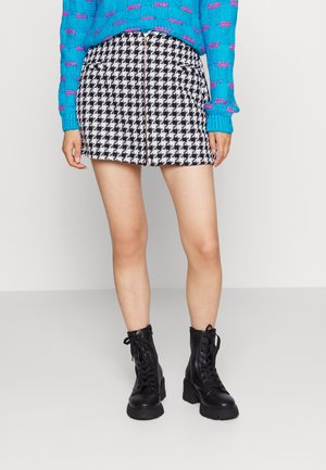 Zwart-wit houndstooth kort rokje met een rits aan de voorkant. Gepaarde met een blauwe gebreide trui en zwarte veterlaarsjes.