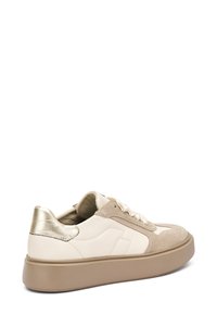 Sneaker con punta in suede beige, parte superiore in pelle crema e accento in metallo dorato sul tallone. Suola in gomma spessa di colore marrone chiaro.