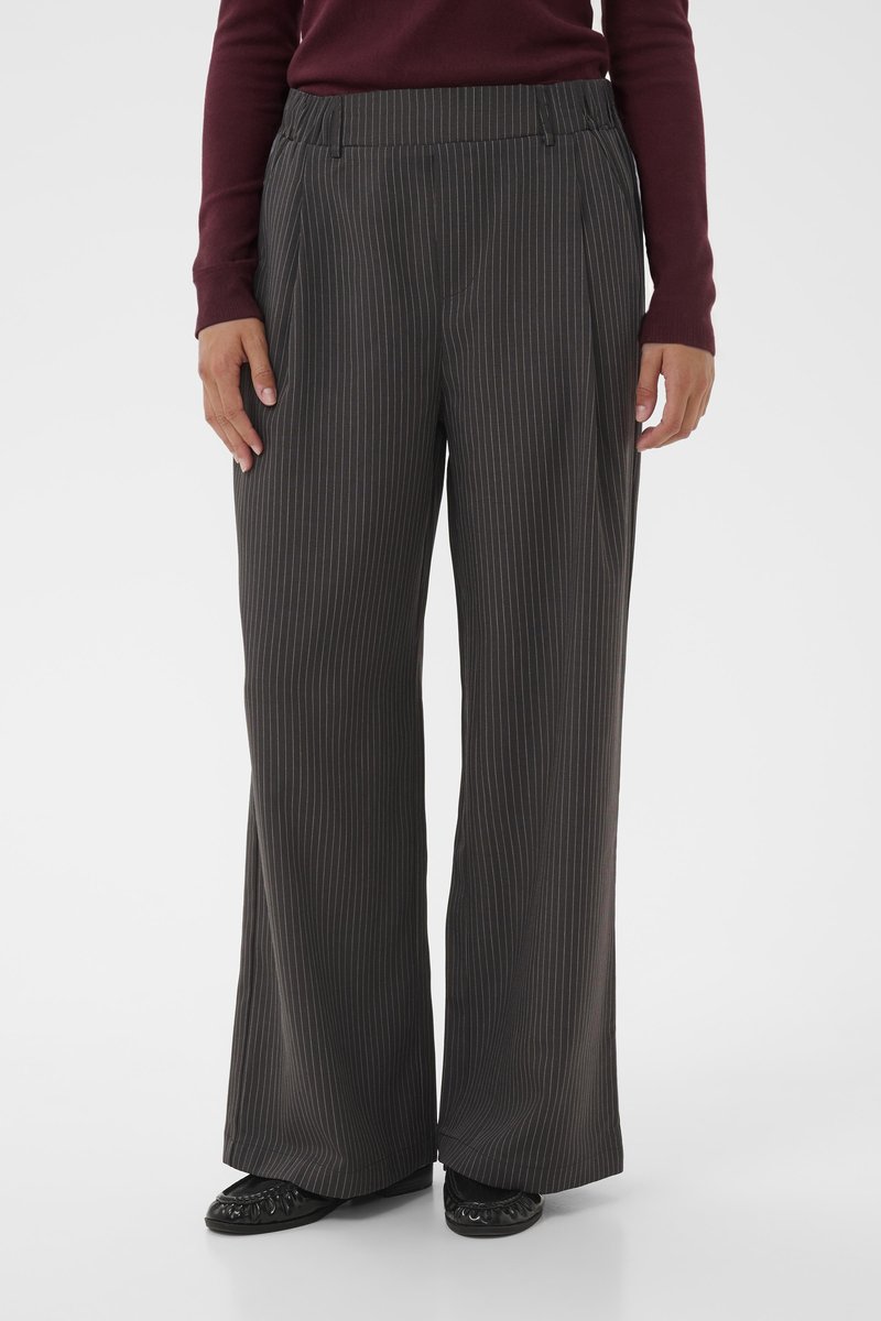 Pantalons à jambes larges en tissu gris foncé à rayures, dotés d'une taille haute, de plis et de poches latérales. Portés avec des chaussures noires.