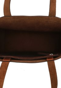 Sac fourre-tout en daim marron, doté d'un intérieur lisse, de deux poignées robustes et d'une poche glissière avec des coutures décoratives le long du bord.