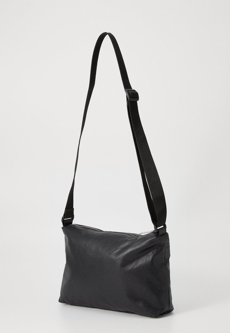Sac messager noir de forme rectangulaire, fabriqué en matériau texturé. Dispose d'une longue bandoulière réglable et d'une fermeture éclair.