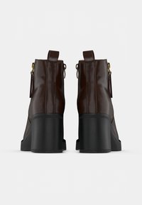 Brūnas ādas potīšu zābaki ar bloka papēdi, sānu rāvējslēdzēju, cilpām un teksturētu melnu gumijas zoli.