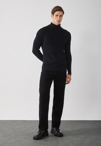 Suéter negro de cuello alto acanalado, combinado con pantalones negros y zapatos de cordones negros. Diseño sencillo con tejido texturizado y ajuste a medida.