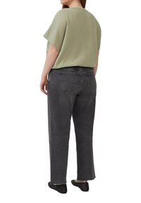Übergroßes, hellgrünes strukturiertes Oberteil, kombiniert mit dunkelgrauen schmalen Jeans. Schwarze Slipper mit Perforationen. Rückansicht.