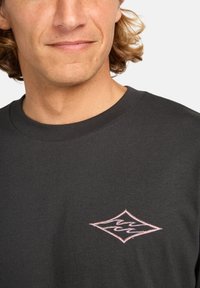 Schwarzes T-Shirt mit kurzen Ärmeln aus Baumwolle, Rundhalsausschnitt und einem rosa gestickten Diamantlogo auf der linken Brust.
