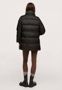 Giubbotto puffer nero con colletto alto e motivo a righe orizzontali. Indossato con leggings marroni e stivaletti neri chunky fino alla caviglia.