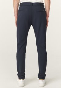 Navyblauwe broek met een slim fit, gemaakt van een zachte stof. Beschikt over twee achterzakken en riemlussen. Eenvoudig, schoon ontwerp.