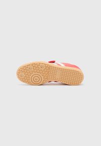 Red sneaker with white stripes, rubber sole featuring a patterned grip, and a velcro strap. Suede upper with a smooth texture.