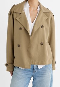 Beige double-breasted jacket with large brown buttons, wide lapels, and shoulder epaulets, layered over a white shirt. Cotton-blend fabric.