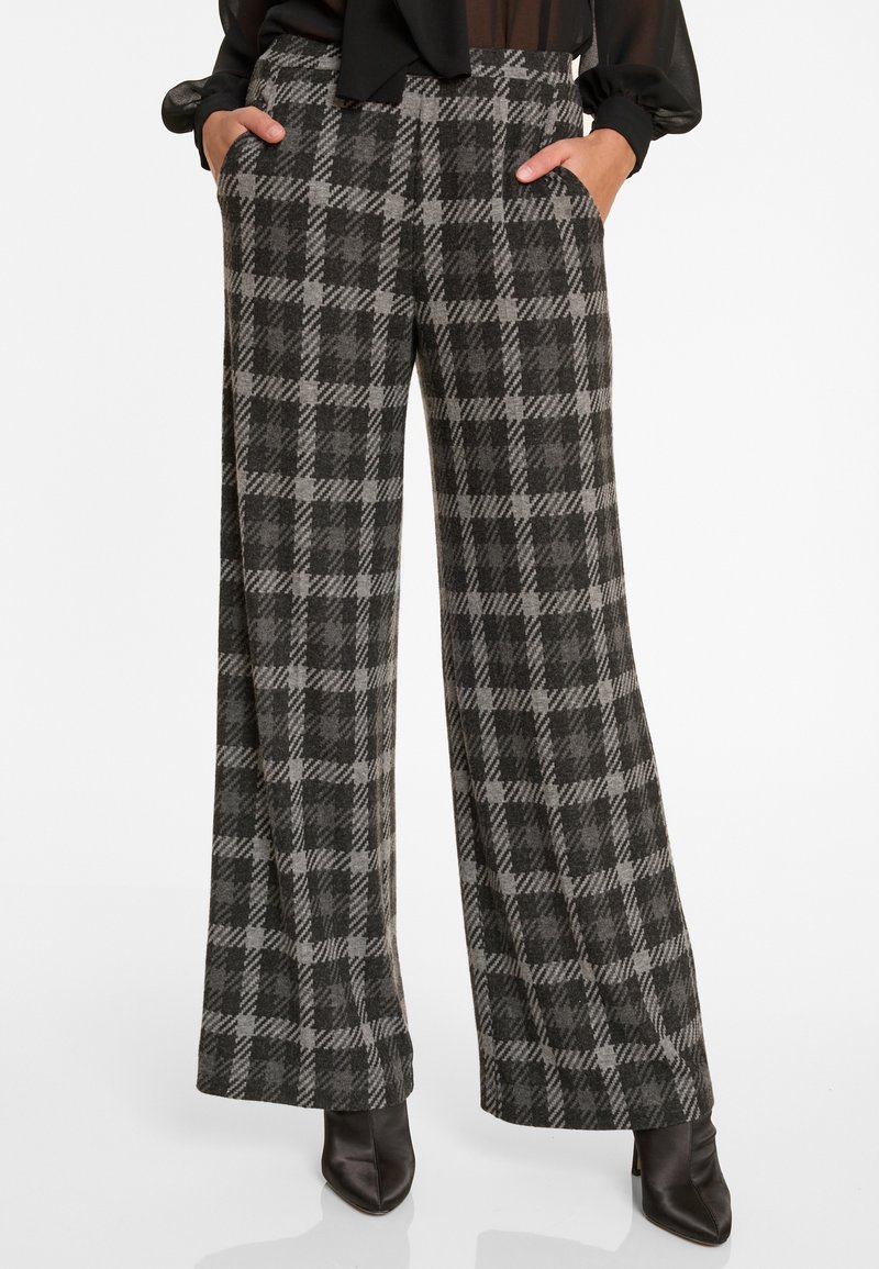 Wijdbenige broek in een zwart-grijs ruitpatroon, met zijzakken en een gladde textuur, gecombineerd met zwarte pumps met een puntige neus.