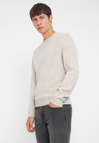 Lysbeige strikket sweater med rund hals, ribbede manchetter og kant. Sammen med mørkegrå jeans, glat tekstur, afslappet pasform.