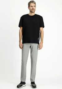 T-shirt nera a maniche corte, vestibilità rilassata, abbinata a pantaloni slim-fit grigio chiaro. Le scarpe sono nere con un accento grigio. Design complessivo semplice.