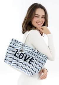 Borsa tote intrecciata in blu, bianco e blu navy. Presenta la scritta "LOVE" in lettere di feltro blu navy, un charm decorativo e una tracolla intrecciata.