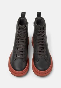 Czarne skórzane sneakersy typu high-top z czerwonymi grubymi podeszwami, sznurowane z przodu, z suwakiem po bokach i uchwytami, na białym tle.