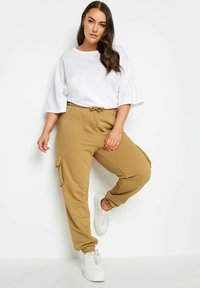 Avslappnad outfit med en vit oversized t-shirt och beige cargobyxor. Byxorna har resårmidja med dragsko och sidofickor.