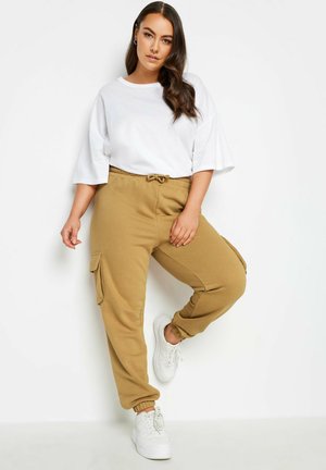 Lässiges Outfit mit einem weißen oversized T-Shirt und beigen Cargo-Hosen. Die Hosen haben einen elastischen Bund mit Kordelzug und seitlichen Taschen.