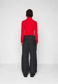 Maglione a girocollo rosso con maniche lunghe abbinato a pantaloni neri a gamba larga. I pantaloni presentano tasche laterali doppie e una fascia elastica in vita.