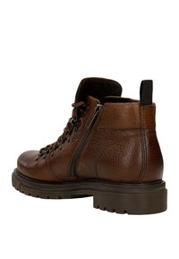 Bruine leren enkelboot met een gestructureerde bovenkant, veters en ritssluiting, en een robuuste zool met een uitgesproken profiel.
