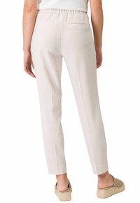 Pantalons tapered beige clair avec une taille élastique et deux poches arrière. Texture lisse, design ajusté et finition soignée.