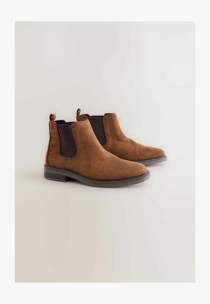 Hnědé semišové Chelsea boots s elastickými bočními panely, kulatou špičkou a kontrastními černými akcenty. Ploché gumové podrážky a poutka pro snadné obutí.