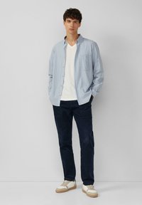Lichtblauw geruit overhemd met knopen over een witte V-hals t-shirt, gecombineerd met marineblauwe broek en witte sneakers met beige accenten.