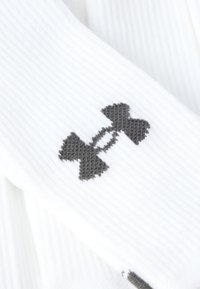 Άσπρες κάλτσες με ριγέ υφή που φέρουν το γκρι λογότυπο Under Armour με μοτίβο μπάρμπελ, δίνοντας έμφαση στην υφή και τις χαρακτηριστικές λεπτομέρειες της μάρκας.