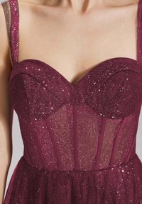 Robe bordeaux en tissu scintillant, avec un corsage transparent, des bonnets moulés et des bretelles fines. Présente des paillettes discrètes sur l'ensemble.