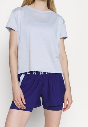 Camiseta corta de color azul claro con mangas cortas, combinada con pantalones cortos morados que tienen una cinturilla blanca y acentos en los paneles laterales.