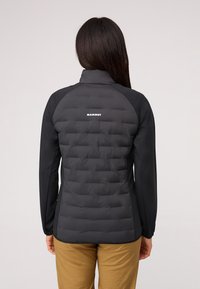 Svart isolerad jacka med puffad design på ryggen och slät tyg på ärmarna. Har en stå krage och logotyp på övre delen av ryggen.