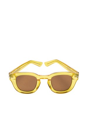 Żółte przezroczyste kwadratowe okulary przeciwsłoneczne z brązowymi przyciemnianymi soczewkami, pokazane na białym tle.