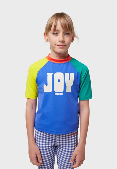 Barn som bär en kortärmad, färgglad rash guard med blå, grön, gul och röd accent. Har "JOY" i fet stil i vita bokstäver.
