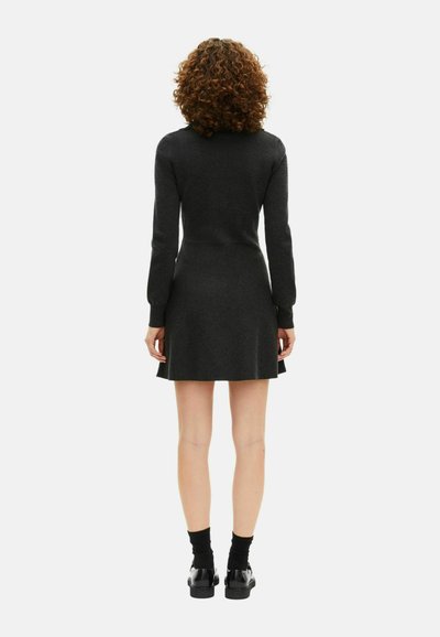 Abito a maglia grigio scuro con maniche lunghe, busto aderente, gonna svasata e polsini a coste, abbinato a scarpe nere chunky e calze.