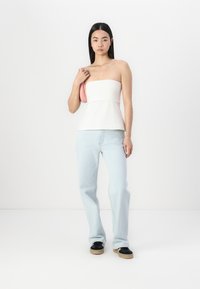 Biely top bez ramienok s peplum pásom, skombinovaný s svetlomodrými džínsy rovného strihu a čiernymi topánkami s béžovými podrážkami.