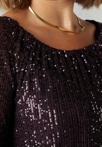 Top viola con paillettes e scollatura arricciata, caratterizzato da una collana in metallo dorato lucido. Il top ha una superficie lucida e testurizzata.