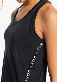 Černý sportovní top s těsným střihem, s kontrastním bočním pruhem s opakovaným textem "ROXY", hladkým texturem a závodním výstřihem.