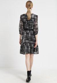 Abito a fantasia nera e grigia con vita aderente, maniche corte a sbuffo e gonna svasata. Tessuto leggero e morbido con una leggera lucentezza.