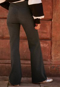 Pantalones acampanados grises en un tejido suave y elástico con una cintura alta. Presenta una textura suave y un diseño minimalista sin patrones ni acentos.