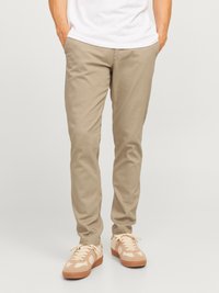 Beige katoenen chinos met een recht gesneden pasvorm, voorzien van zijzakken en een zachte textuur. Gekleed met lichtgekleurde sneakers.
