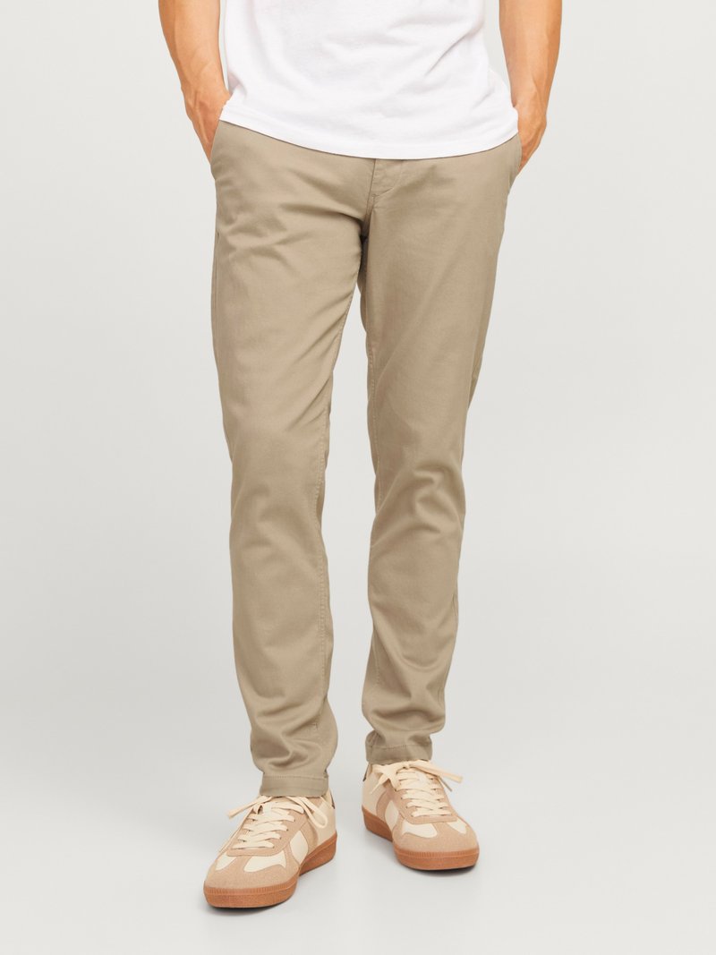 Beige katoenen chinos met een recht gesneden pasvorm, voorzien van zijzakken en een zachte textuur. Gekleed met lichtgekleurde sneakers.