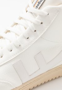 Białe sneakersy z teksturowanej skóry, płaskimi białymi sznurówkami i beżową gumową podeszwą. Posiadają duże białe litery z boku.