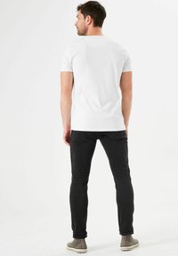 Camiseta blanca de manga corta combinada con jeans ajustados negros y botas de tobillo grises. El conjunto presenta un diseño sencillo sin patrones visibles.