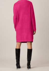 Vestito maglia rosa oversize con texture a coste, maniche lunghe e scollo rotondo, abbinato a stivali neri in pelle al ginocchio.