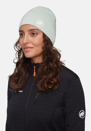 Berretto azzurro chiaro con una texture liscia, dotato di un logo sulla parte frontale. Abbinato a una giacca nera a righe con dettagli arancioni nella zip.