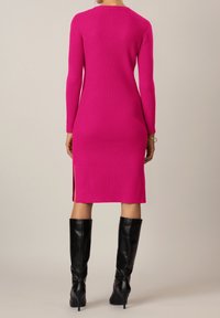 Vestito aderente rosa a coste con maniche lunghe e spacchi laterali, abbinato a stivali neri con tacco al ginocchio. Tessuto liscio, leggermente elasticizzato.