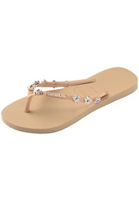 Sandal cu talpă texturată, de culoare bej, cu bretele împletite decorate cu accesorii argintii în formă de floare și mici nituri metalice.