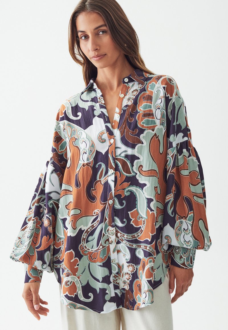 Camisa de botones con mangas largas y anchas en un patrón de paisley multicolor de verde, naranja y azul marino sobre un fondo claro. Tejido texturizado.