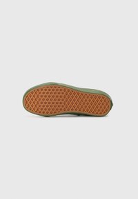Suela de zapatilla verde con un fondo de goma naranja texturizado, que presenta un patrón de diamante para mayor agarre y un borde superior liso.