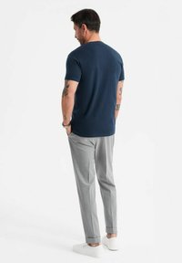 T-shirt a maniche corte blu navy abbinato a pantaloni grigi chiari e scarpe bianche senza lacci, visto da dietro.