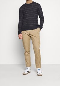 Pull bleu marine avec un motif texturé, chinos beiges et baskets blanches avec des rayures noires et des accents bleus. Tenue simple et décontractée.
